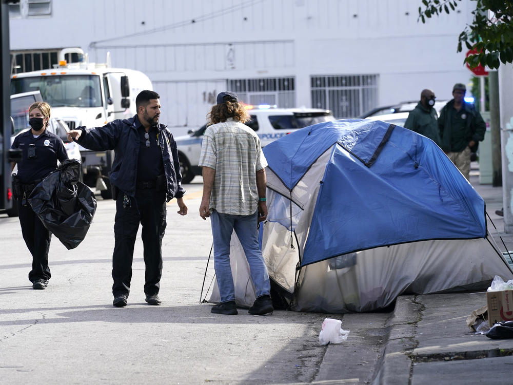 A Miami police officer talks with a homeless person, prior to a cleaning of the street in 2021. Starting October 1st, a new law will ban Florida's homeless from sleeping in public spaces.