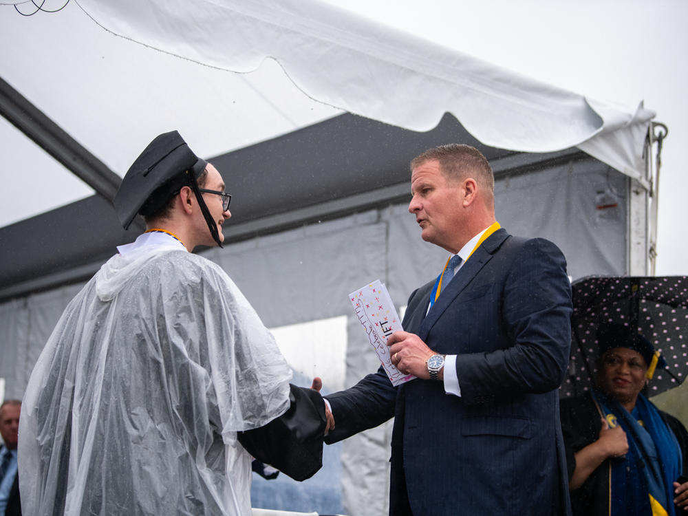 Robert Hale gives an envelope with cash to a graduating UMass Dartmouth student at last week's commencement. Each of the 1,200 graduates received $1,000 onstage, half to keep and half to donate.