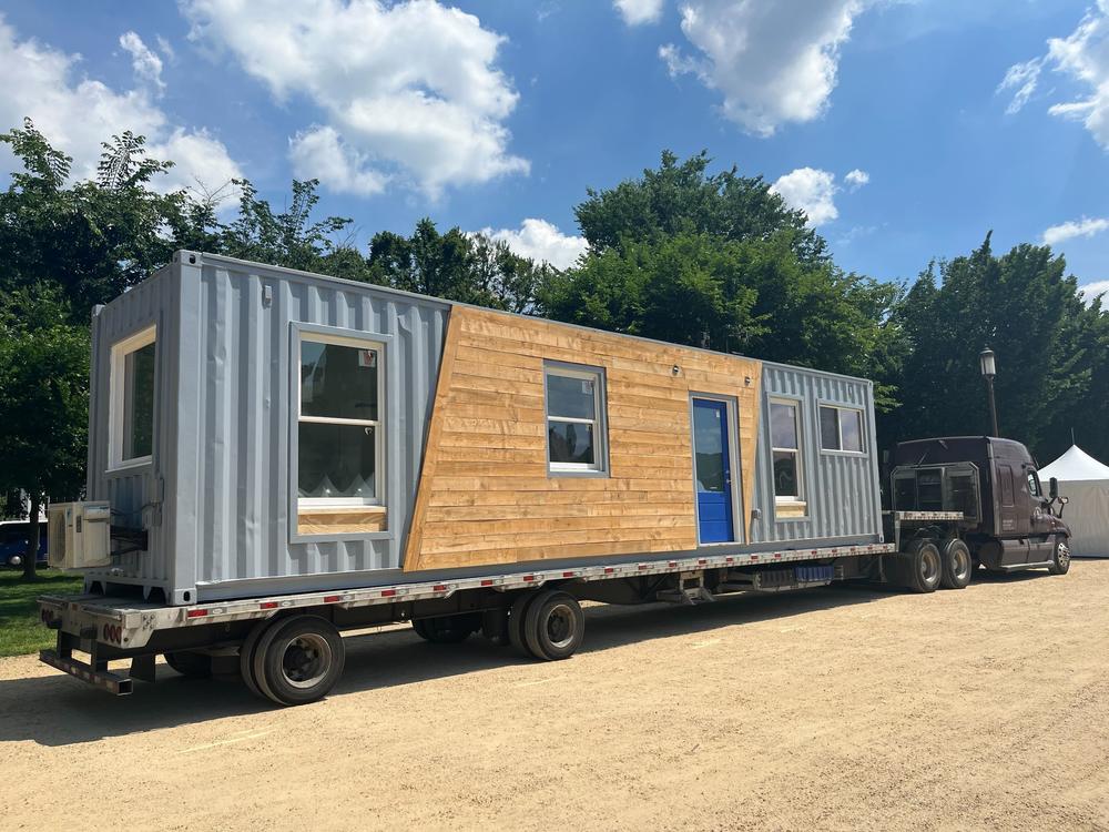 A tiny house made from a shipping container arrives on the Mall, transported by truck.