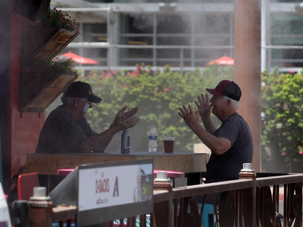 People chat while having drinks under a mister at a restaurant in Phoenix on Wednesday. According to the National Weather Service, Phoenix will experience record temperatures soaring over 100 degrees due to a heat dome stemming from high pressure in the atmosphere. 