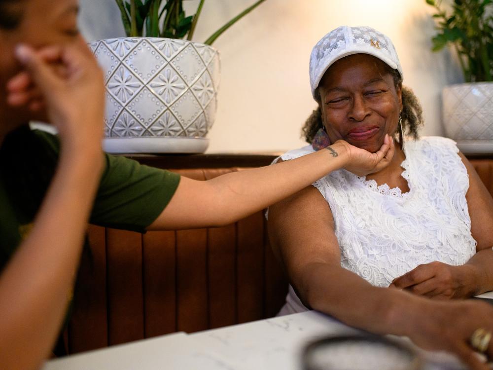 Williams smiles as her daughter, Lena Powell, holds her face while they share a coffee. When Williams lost her SSI checks, she got by with help from her children and friends.