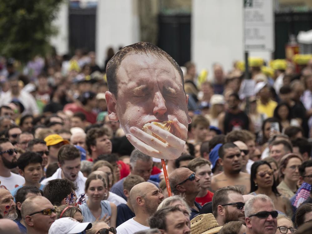 A spectator holds a sign with Joey Chestnut's face during the 2023 Nathan's Famous Fourth of July hot dog-eating contest.