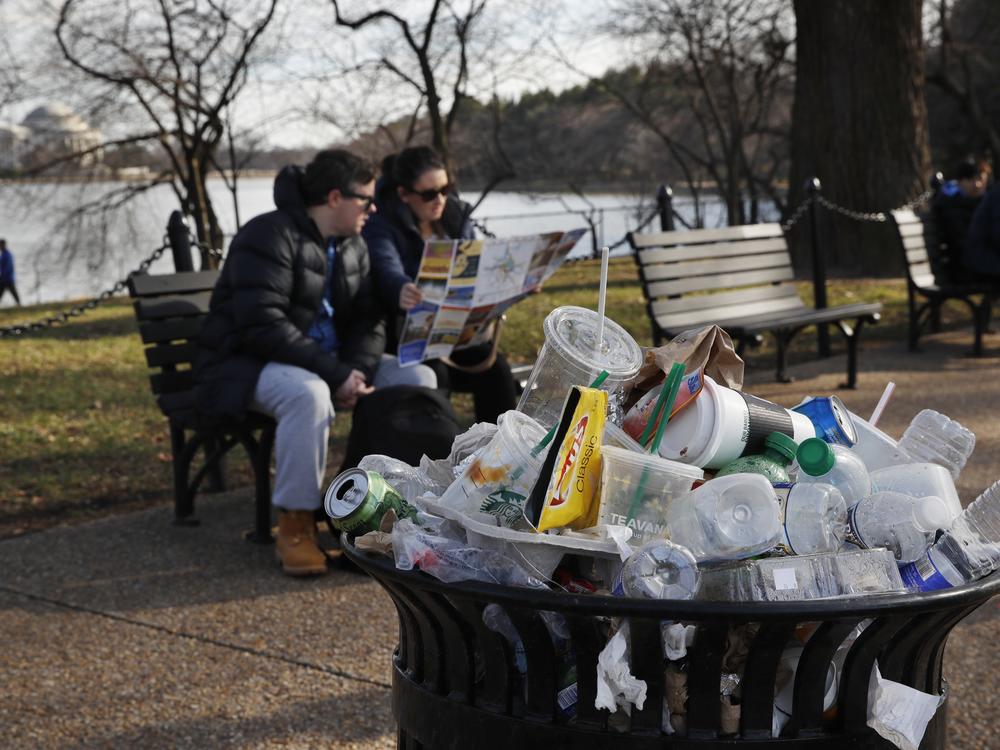 A trash can overflows as people sit outside of the Martin Luther King Jr. Memorial in Washington, D.C.