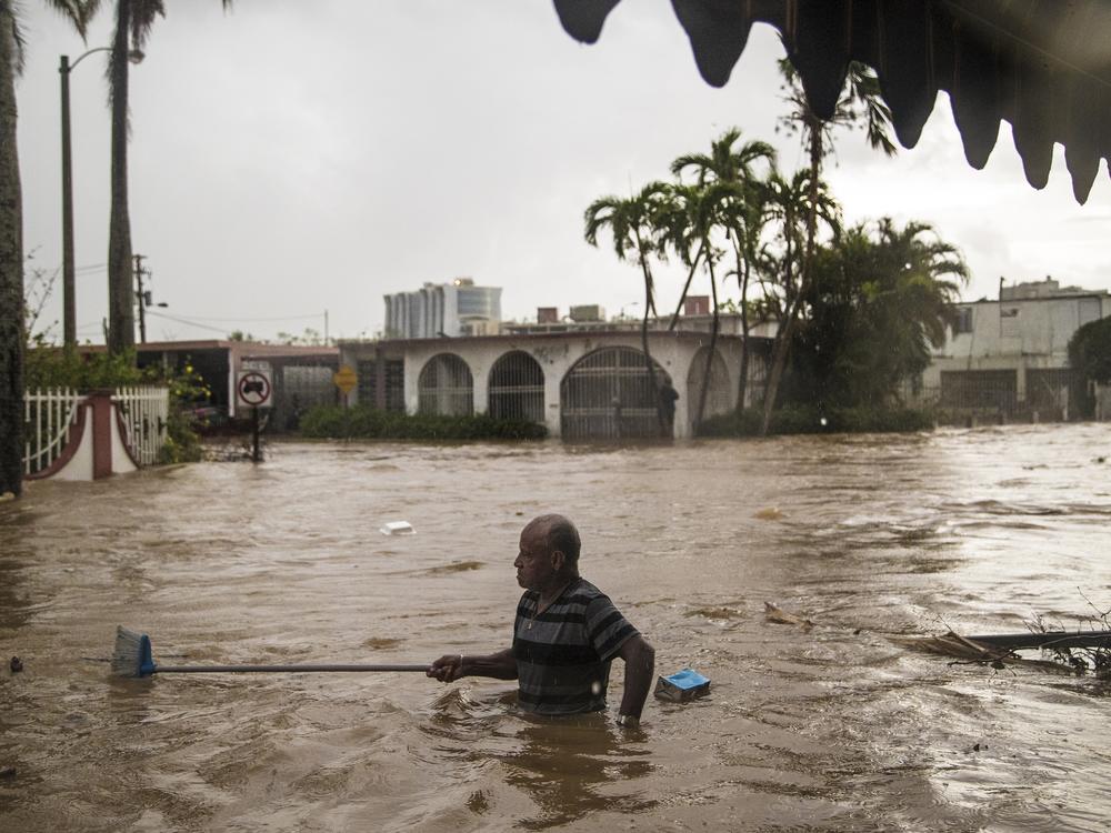 Maximiliano Encarnacion uses a broom to push through floodwaters from Hurricane Maria in San Juan, Puerto Rico, in 2017. The initial official death toll from the storm was in the dozens, but subsequent epidemiological analyses suggested that thousands of additional deaths had gone uncounted.
