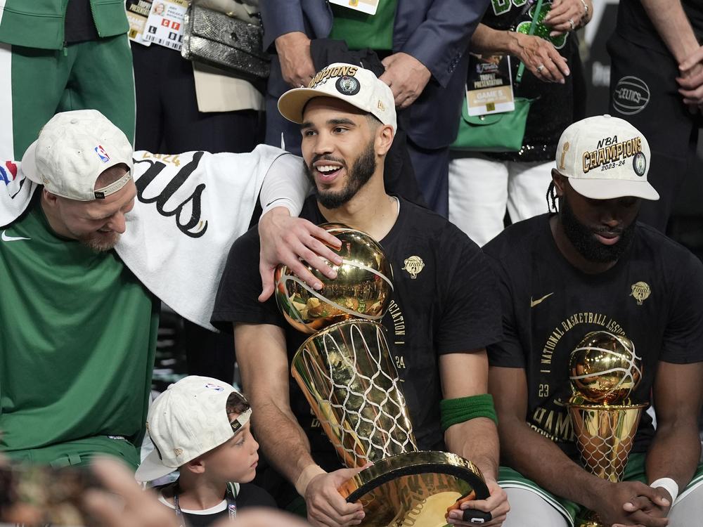 Boston Celtics forward Jayson Tatum, center, holds the Larry O'Brien Championship Trophy as he celebrates with center Kristaps Porzingis, left, and guard Jaylen Brown, right, after the Celtics won the NBA championship with a Game 5 victory over the Dallas Mavericks on Monday in Boston.