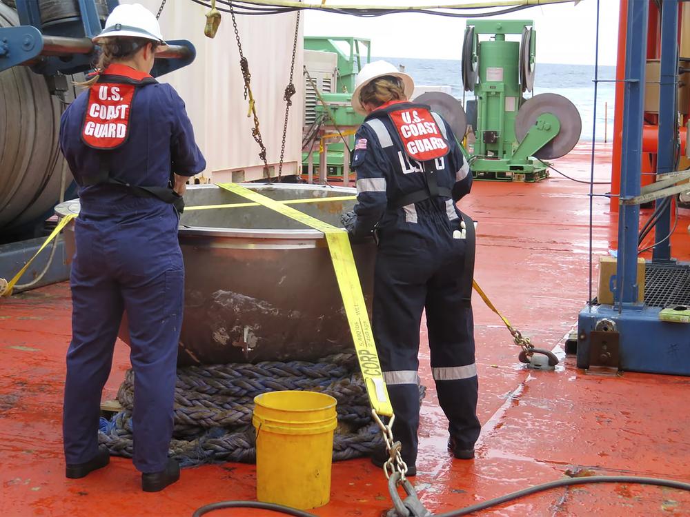 In this photo provided by the U.S. National Transportation Safety Board, U.S. Coast Guard marine safety engineers survey the aft titanium endcap from the Titan submersible, in the North Atlantic Ocean in October 2023.