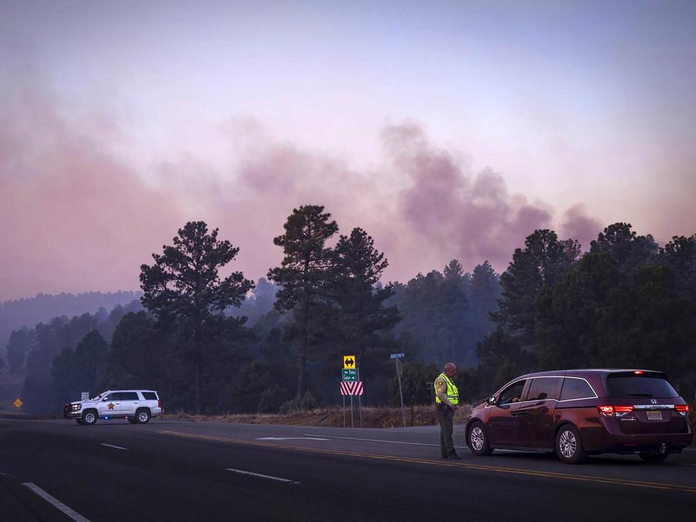 Smoke from the South Fork Fire reflects a pink hue during sunrise Tuesday as law enforcement officers turn drivers away on State Road 48 at State 220 because of wildfires burning near Ruidoso, N.M. 