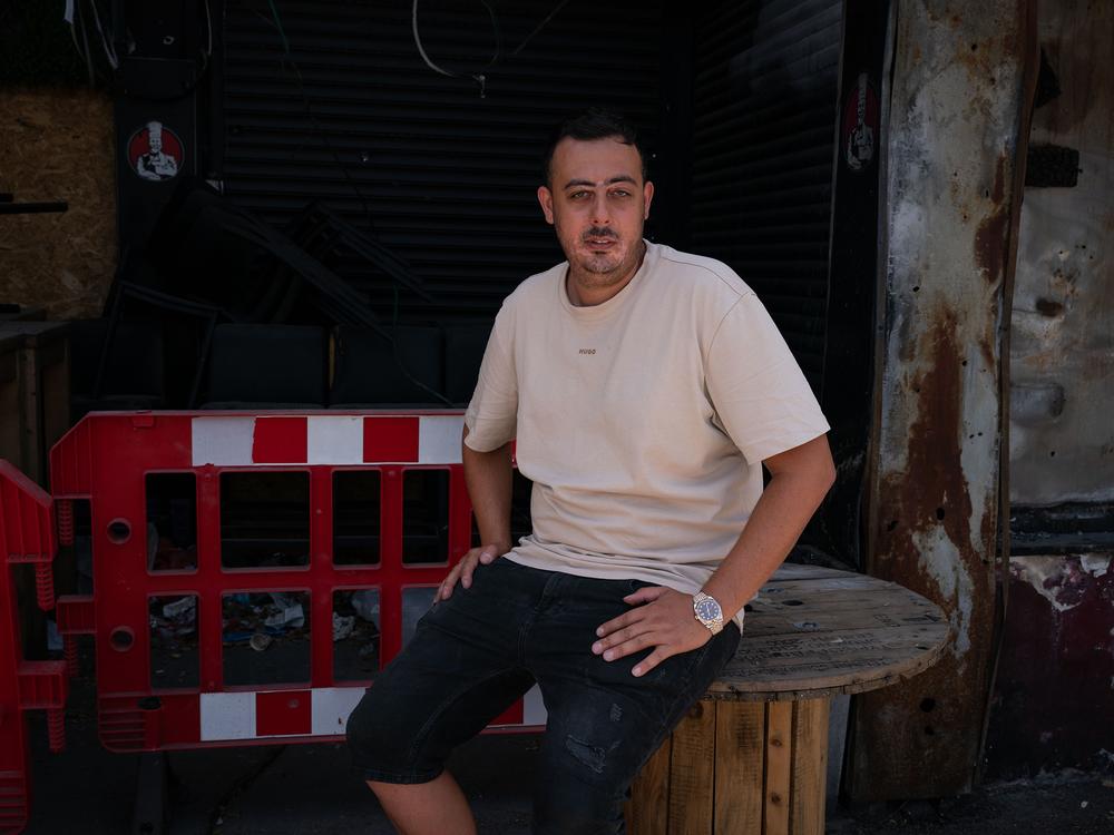 Asaf Maman, 31, sits in front of the burned wreckage of a shawarma restaurant he owns that was hit by a Hezbollah rocket in early November 2023, in the Israeli town of Kiryat Shmona. He was working in the restaurant when the rocket hit. He says his 25-year-old brother was wounded in the stomach from shrapnel and is still recovering. 