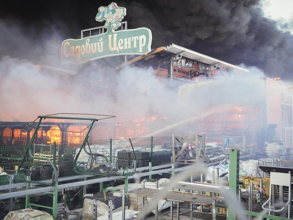 Firefighters try to put out a fire after two guided bombs hit the Epicenter shopping complex in Kharkiv, Ukraine, on Saturday, May 25, 2024. The sign reads 