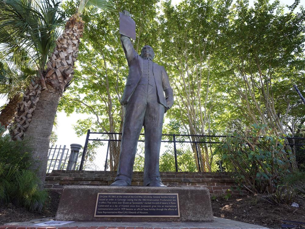 In this June 17, 2020, photo, a statue depicts a man holding the state law that made Juneteenth a state holiday in Galveston, Texas. 
