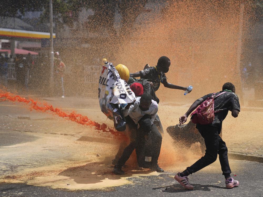 Protesters scatter as Kenyan police spray water canon at them during a protest over proposed tax hikes in a finance bill in downtown Nairobi, Kenya, on Tuesday.
