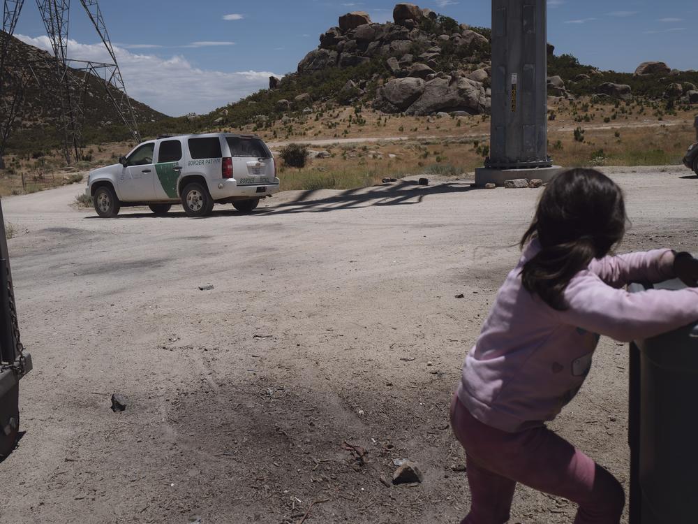 A border patrol agent approaches the informal migrant camp in Jacumba Hot Springs, California, as a child washes her hands on June 24, 2024. 