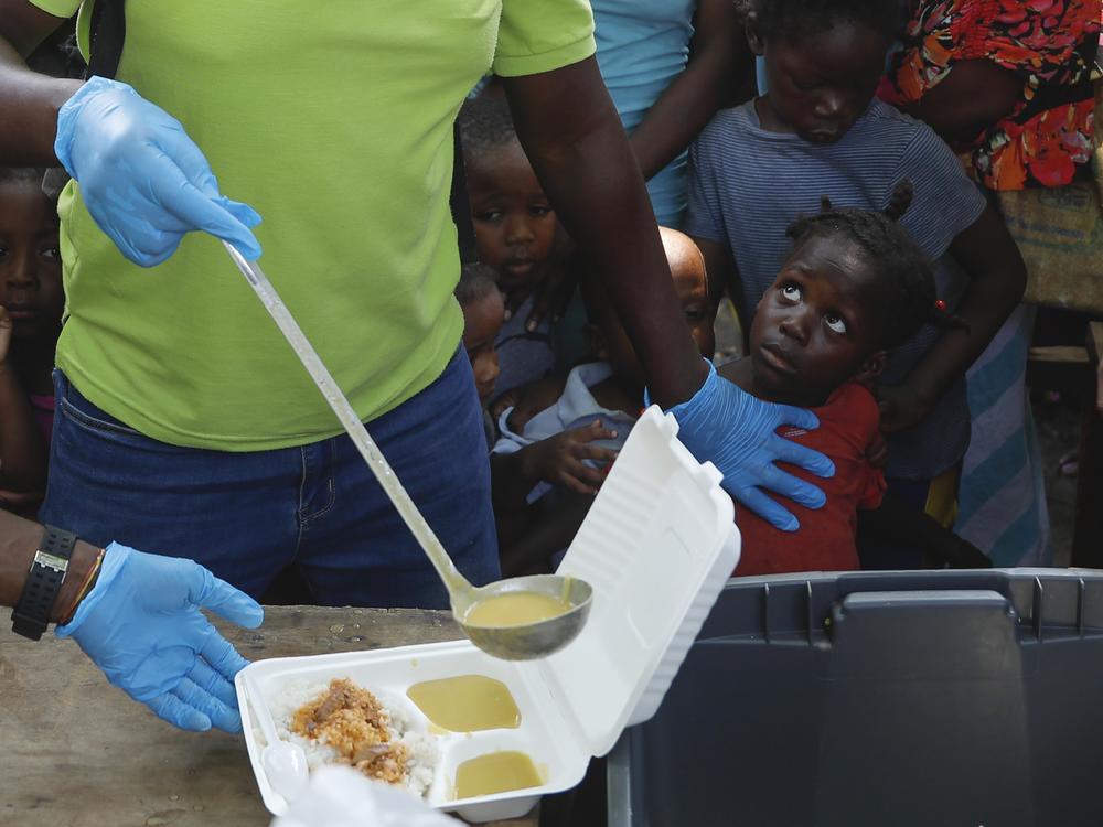 A server ladles soup into a container as children line up to receive food at a shelter for families displaced by gang violence, in Port-au-Prince, Haiti, in March 2024. Gang violence in Haiti has displaced over 300,000 children since March, according to a new report from the U.N. children's agency released late Tuesday.