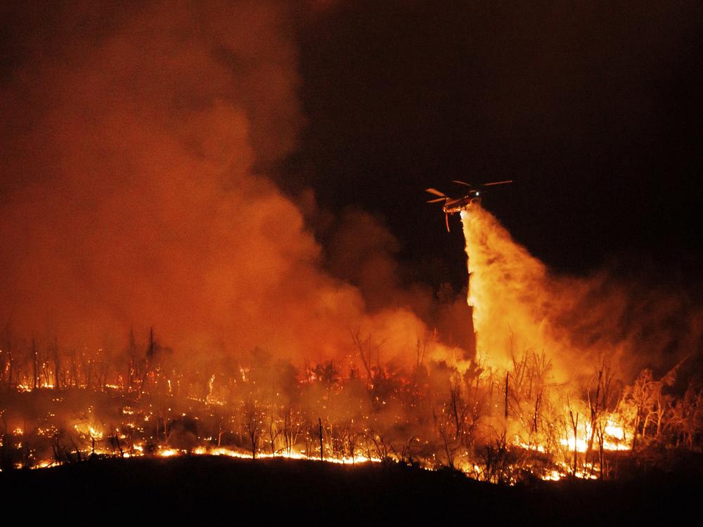 A night flying helicopter drops water on flames as the Thompson Fire burns Tuesday in Oroville, Calif. 