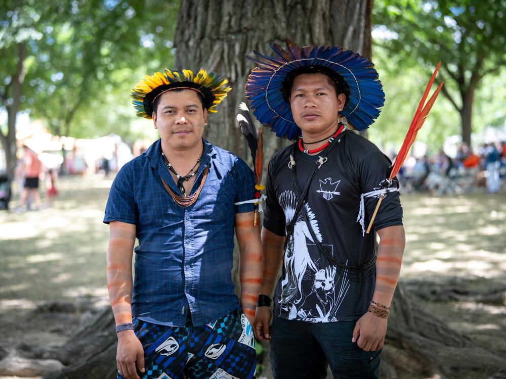  Tambura Amondawa (left) sports the bright yellow-orange feathers of the macaw that is their symbol of his clan. At right is Tupi Kawahin, who wears the deep blue feathers of his clan's mutuanaguera bird symbol. Together they sang a song, composed by Tambura's grandfather, celebrating the survival of their Indigenous community.<br>