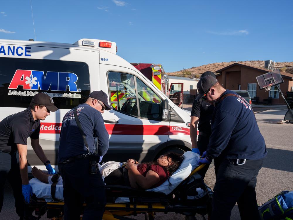 Sunland Park Fire Department firefighters and police officers roll a migrant woman, who was suffering from heat-related illness, on a gurney to be loaded into an ambulance in a residential area in Sunland Park, N.M., on Friday, June 28, 2024.
