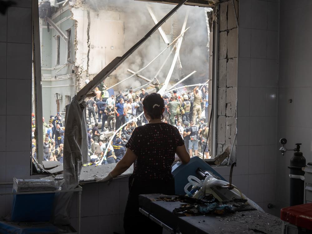 A health care worker looks through a window of a damaged operating room as people clear rubble at the building of one of Ukraine's largest children’s hospitals, Okhmatdyt, partially destroyed by a Russian missile strike on Monday.