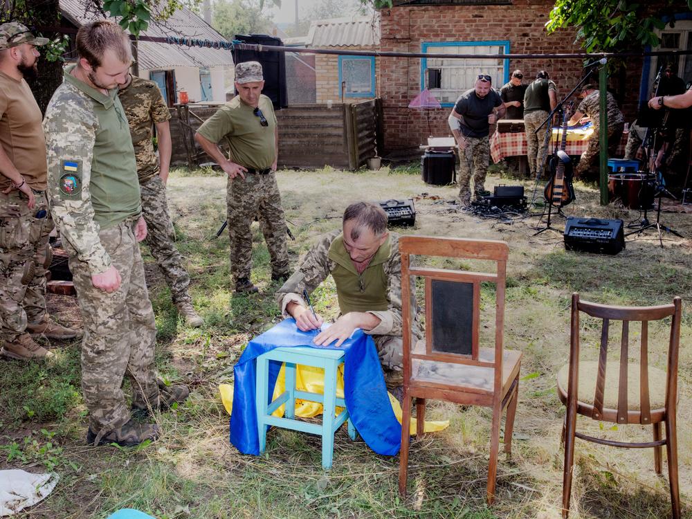 After a band of soldiers plays a concert for fellow troops near the front lines, the whole unit who attended signs a flag for the band.