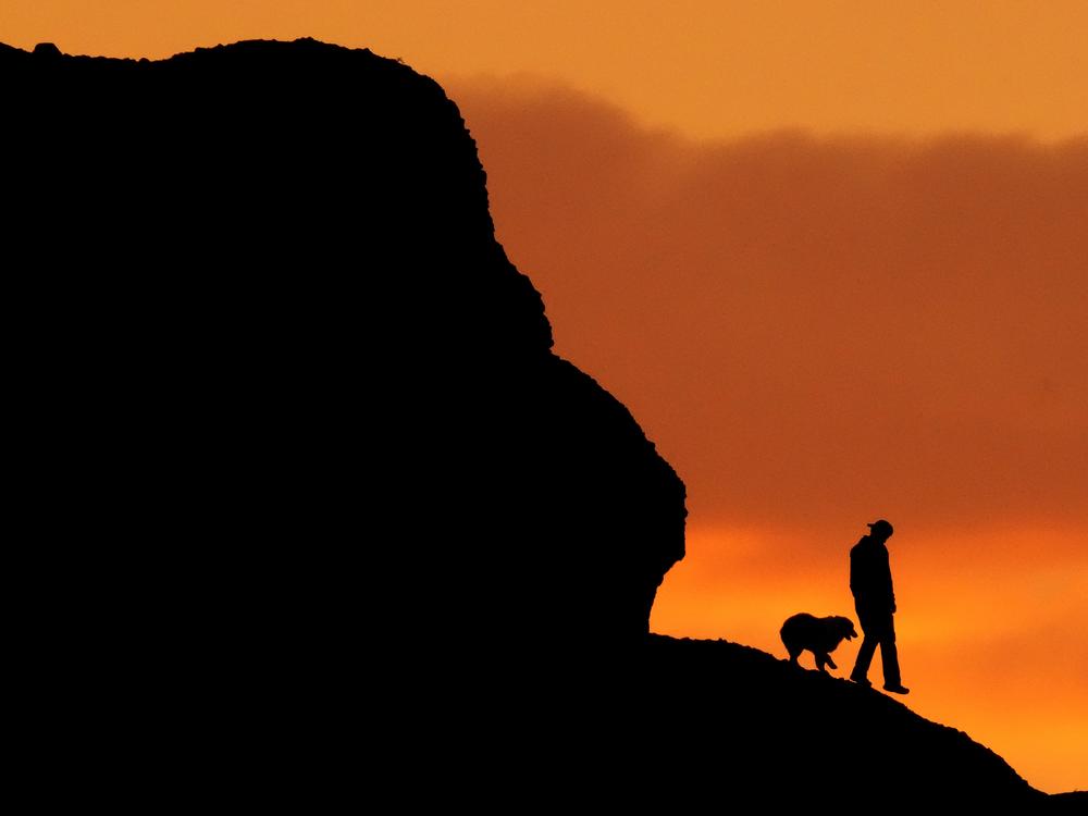 A man and a dog are silhouetted against the sky at sunset as they hike along a ridge at Papago Park in Phoenix on March 2, 2023.
