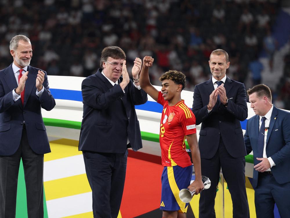 Spain's forward, Lamine Yamal, holds the trophy for best young player and celebrates on the podium next to Spain's King Felipe VI (left) and UEFA President Aleksander Ceferin (right), after winning the UEFA Euro 2024 final soccer match between Spain and England at the Olympiastadion in Berlin on Sunday.