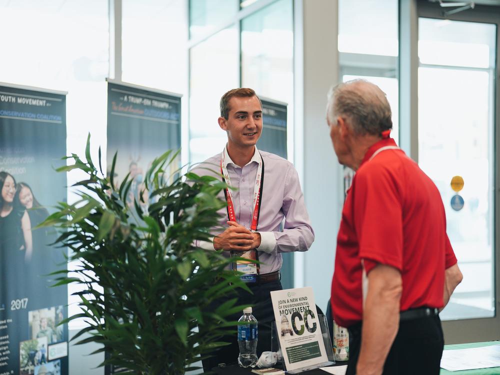  Aidan Shank talking to a guest at the ACC Exhibition booth in Baird Center.
