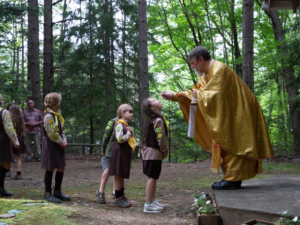 A priest distributes communion by using a golden chalice and a spoon to drop a wine-soaked piece of bread into each person's mouth.