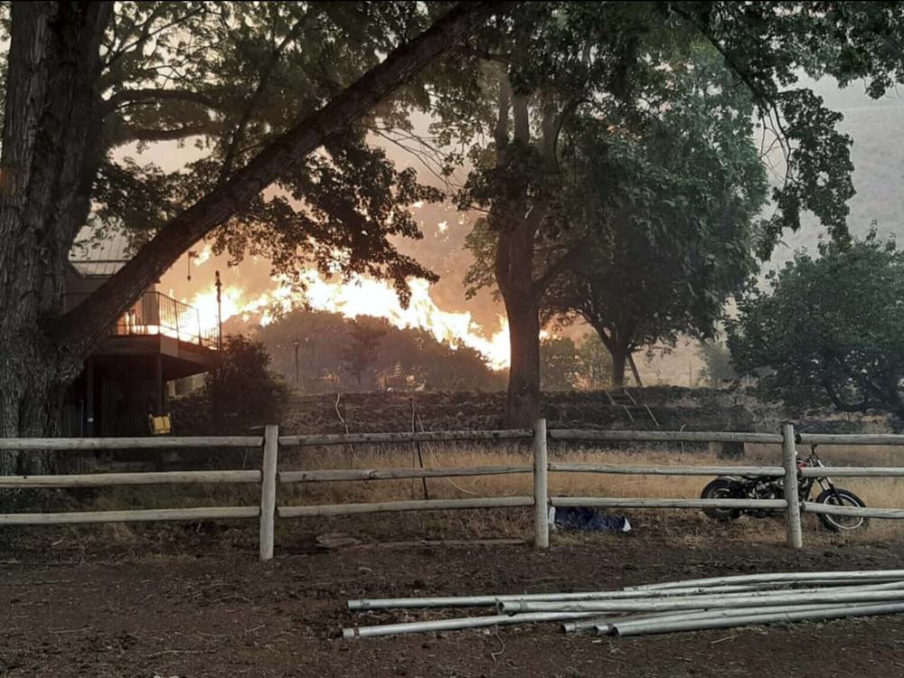 In this photo provided by Alison Oszman, a fast-moving wildfire near the Oregon-Idaho border moves toward a home on Rye Valley Lane in Huntington, Ore., on Wednesday afternoon.