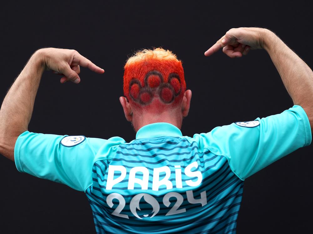 A spectator gestures as the Olympic rings are seen dyed into their hair.