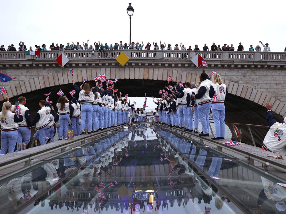 Spectators cheer as Athletes of Team Great Britain pass under a bridge.