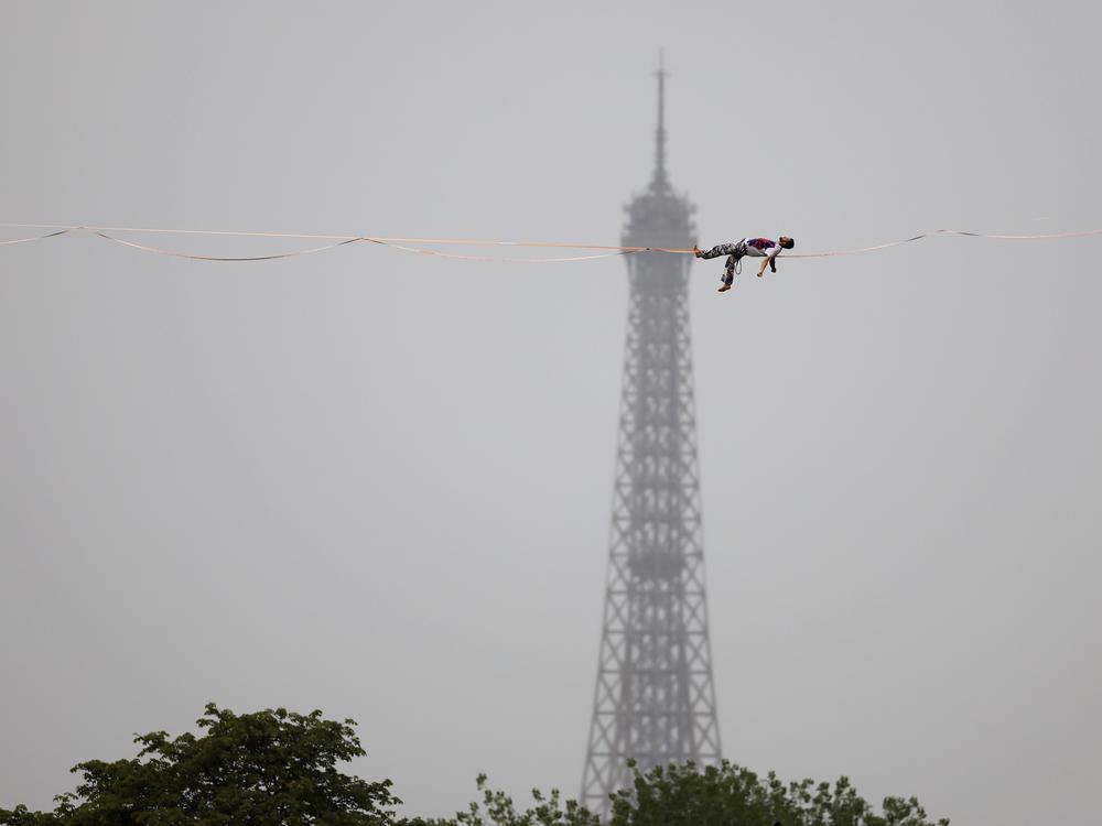 Tightrope walker Nathan Paulin performs on a high rope during the athletes parade on the River Seine.