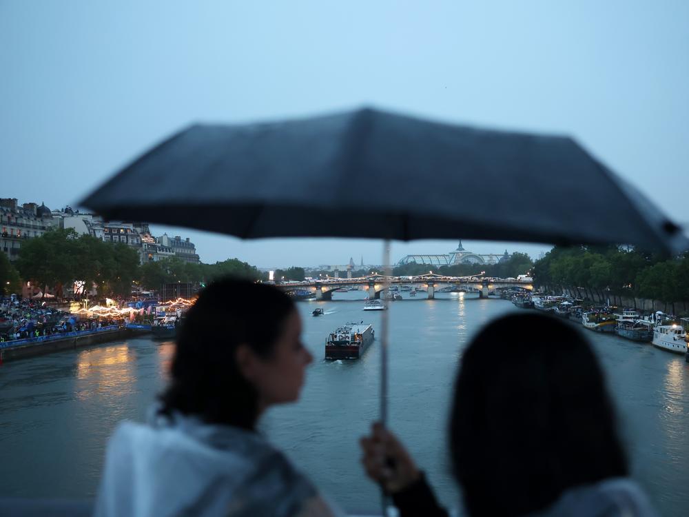 Athlete boats travel along the River Seine as spectators shelter from the rain.