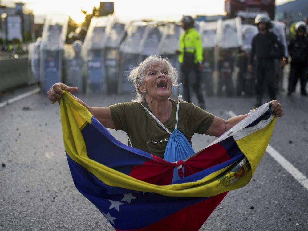 Consuelo Marquez holds a Venezuelan flag in front of police blocking demonstrations against the official election results declaring President Nicolás Maduro's reelection, the day after the vote in Caracas, Venezuela, Monday.