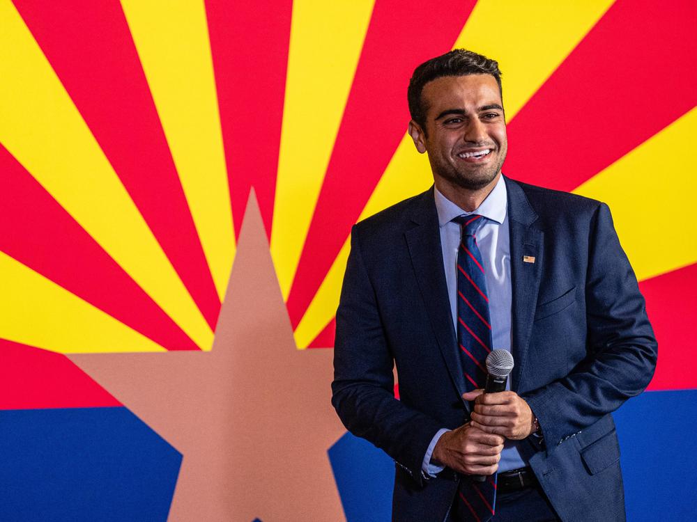 Abe Hamadeh stands in front of an Arizona state flag during a 