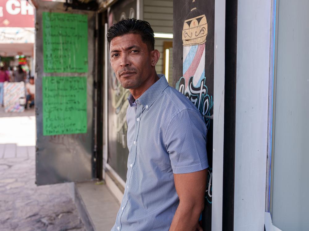 Grebi Suárez, 40, from Venezuela, stands in front of a barber shop where he’s working in Ciudad Juarez, Chihuahua state, Mexico on Saturday, June 29, 2024. Suarez is waiting for an appointment via the CBP One application, part of a growing number of migrants in the city doing so.   