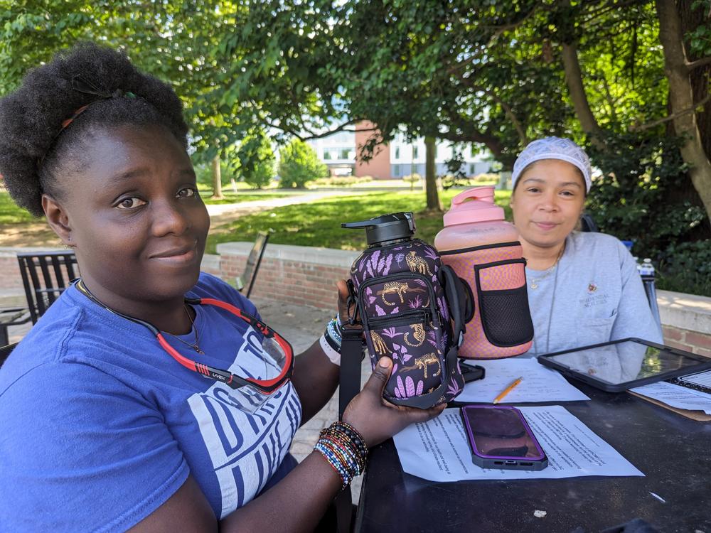 Admire Stewart and Margie Rodriguez hold up water bottles that Rodriguez purchased for housekeepers at the University of Maryland. Hydration is a challenge when the housekeepers work long hours in unairconditioned dormitories across campus.