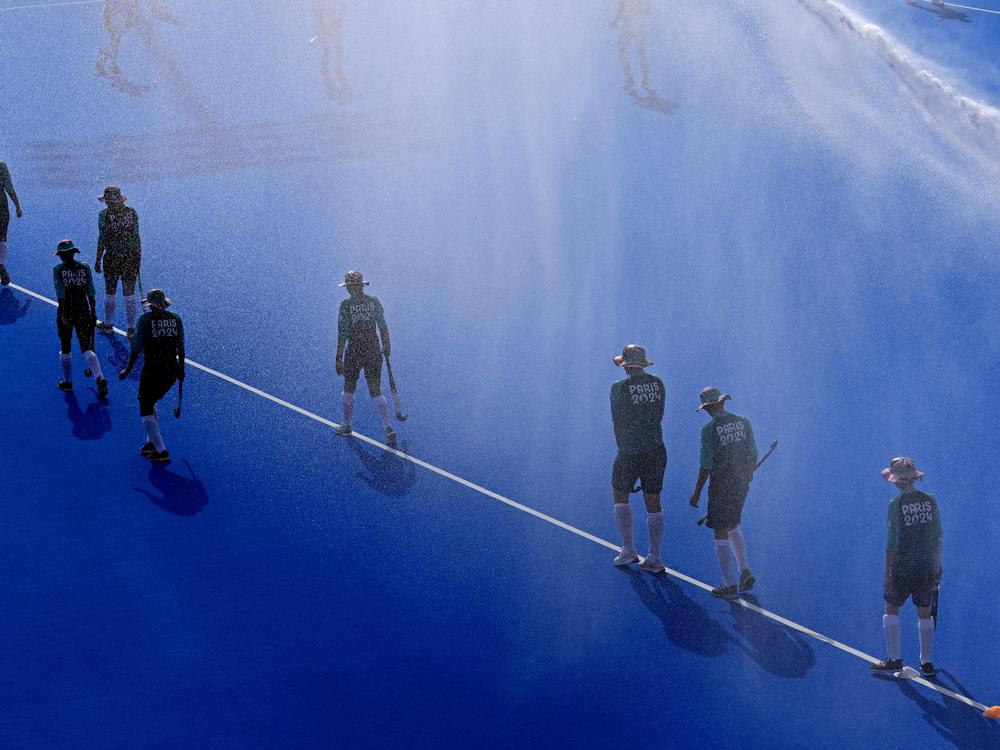 Water is sprayed on the pitch as the ball boys and girls walk along the center line before the start of the men's Group A field hockey match between South Africa and Germany on Tuesday.