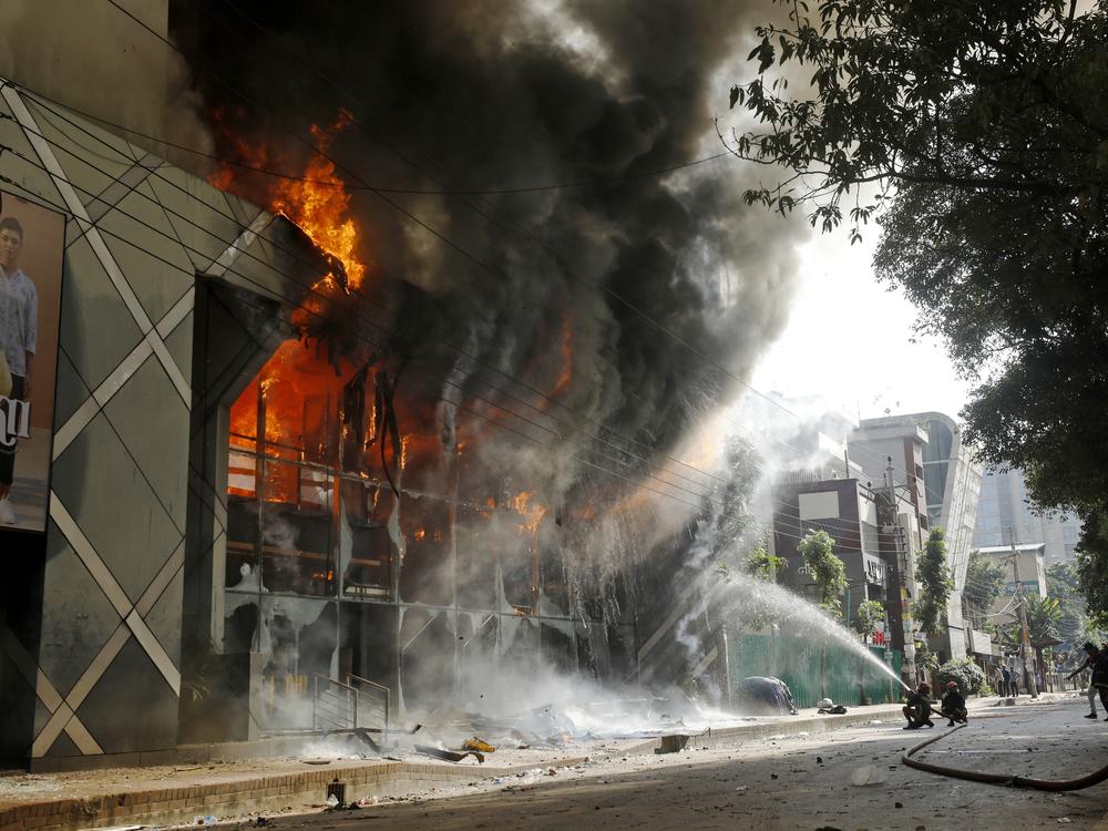 Firefighters douse a fire engulfing a shopping center which was set on fire by protesters during a rally against Prime Minister Sheikh Hasina and her government in Dhaka, Bangladesh. 