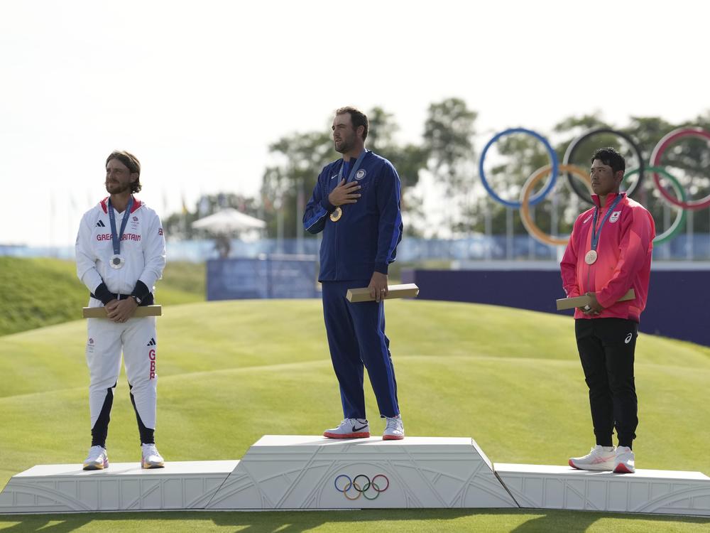 Gold medalist Scottie Scheffler, center, with silver medalist Tommy Fleetwood, left, and bronze medalist Hideki Matsuyama listen to the nation anthem of the U.S. during the medal ceremony for men's golf.
