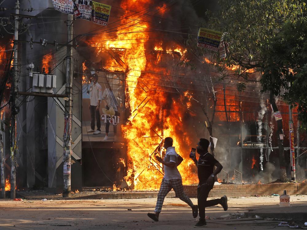 Men run past a shopping center which was set on fire by protesters during a rally on August 4.