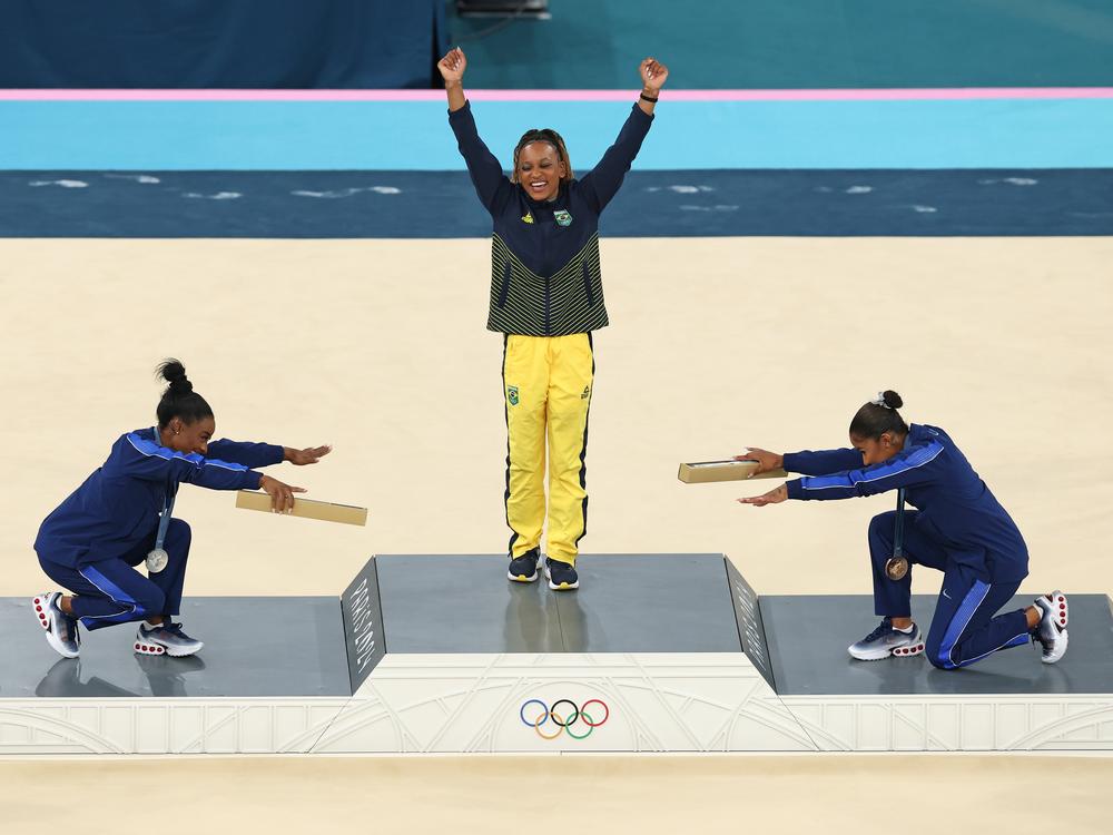 Gymnast Rebeca Andrade (center) of Brazil wins her first gold medal in Paris. Paying homage are silver medalist Simone Biles (left) and bronze medalist Jordan Chiles of the United States. 