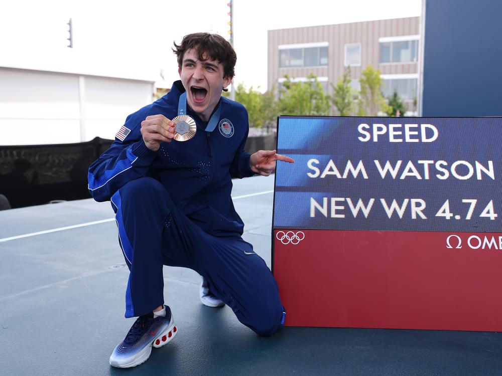 Sam Watson of Team USA poses with his bronze medal alongside a screen with his world record time of 
