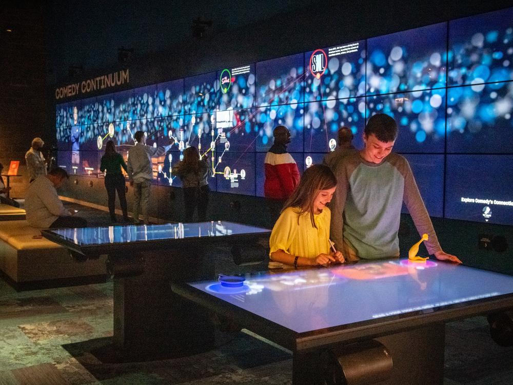 An interactive exhibit at the National Comedy Center invites visitors to select from a shelf full of objects — a frying pan, a banana, an anvil, a rubber chicken. When you place the object on the table and it triggers a video that shows all of the different comedy bits that have incorporated that prop across time and genre.