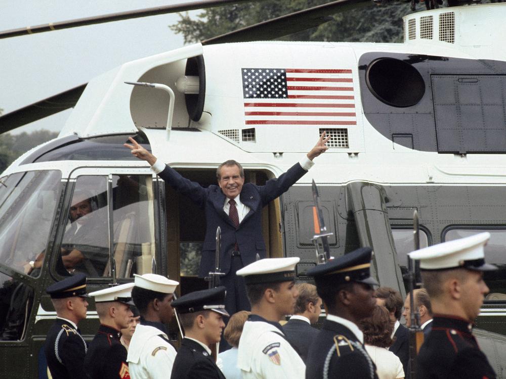 As he boards the White House helicopter after resigning the presidency, Richard Nixon smiles and gives the victory sign.