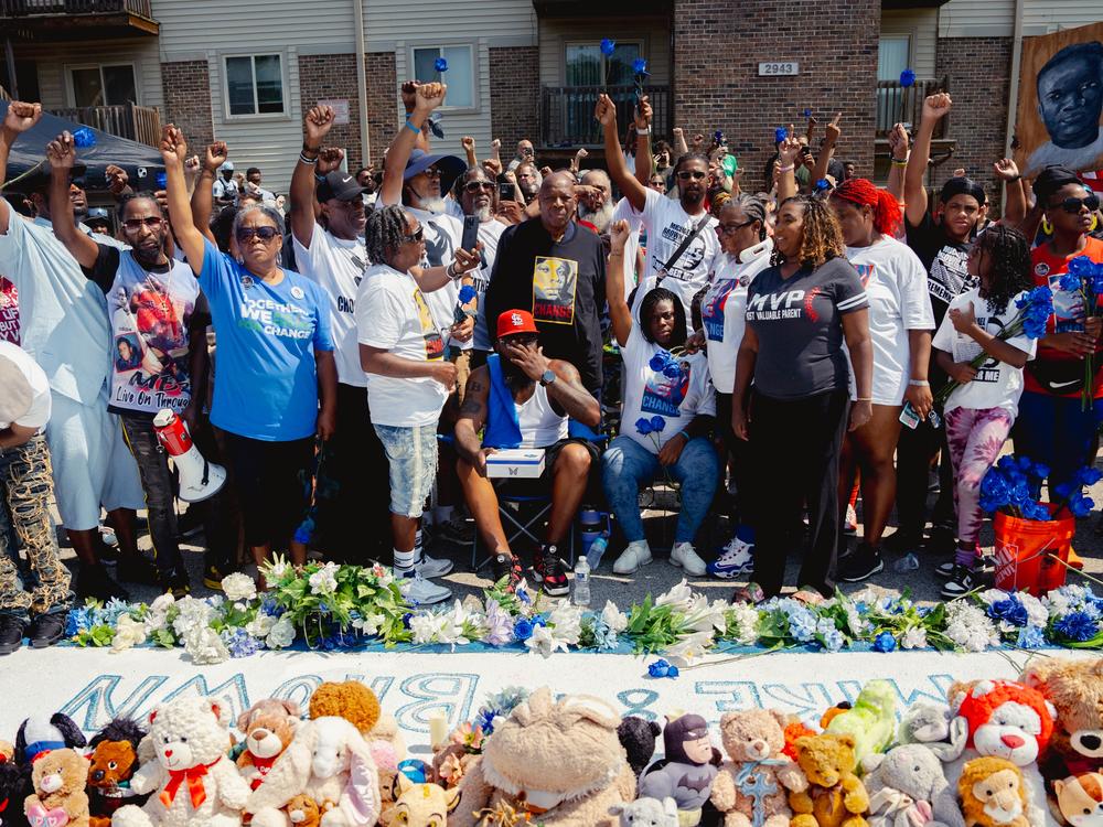 Community activists raise their fists as Michael Brown Sr., center in St. Louis Cardinals hat, wipes his face.
