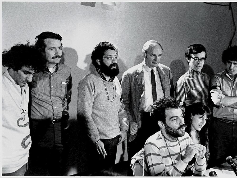 American political activists and anti-war demonstrators known as the Chicago Seven speak to reporters at a press conference after being charged with contempt of court during their trial for conspiracy to incite violence at the 1968 Democratic National Convention, Chicago, Oct. 8, 1969. Standing left to right, Abbie Hoffman, John Froines, Lee Weiner, David Dellinger, Rennie Davis, and Tom Hayden; seated, center, Jerry Rubin; beside him is Nancy Kurshan.