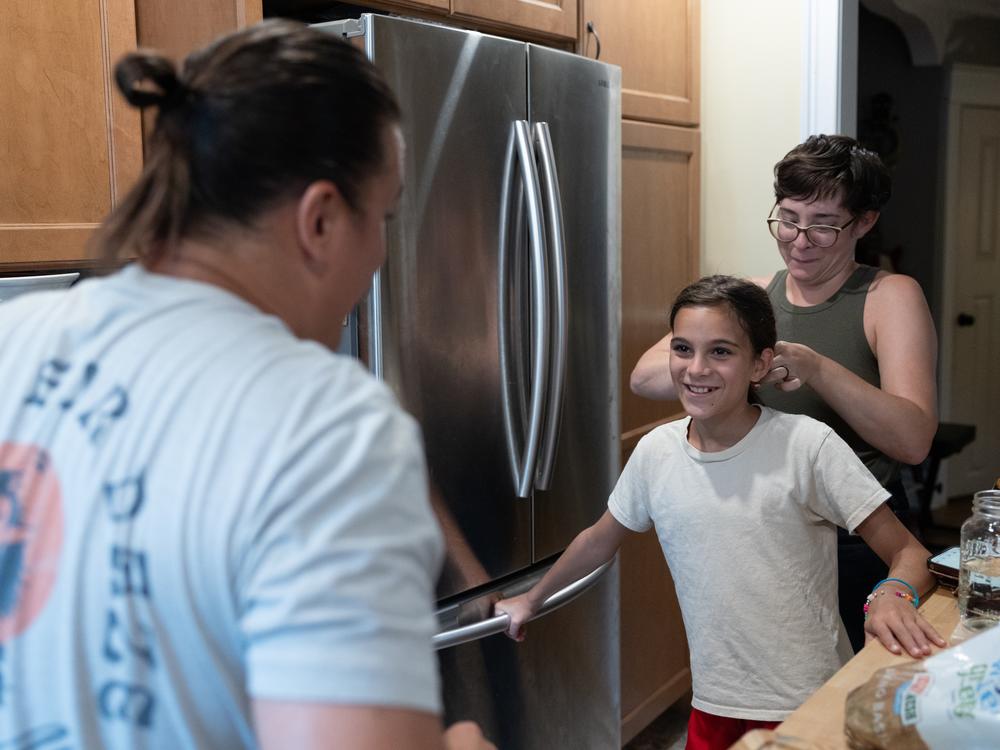 Andrew DiDonato looks on as his wife Ashley pulls their daughter Rosalie's hair back to match her dad's in their home in Philadelphia on July 22, 2024.