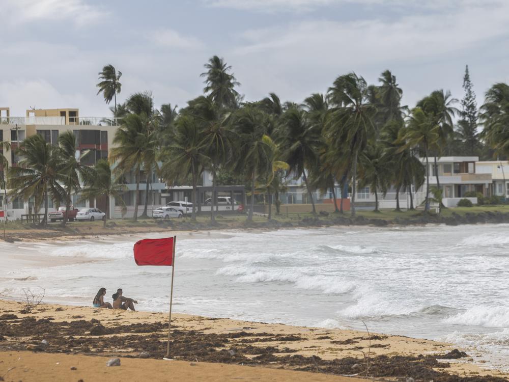 Tourists sit on La Pared beach as Ernesto passes by Luquillo, Puerto Rico, on Tuesday.