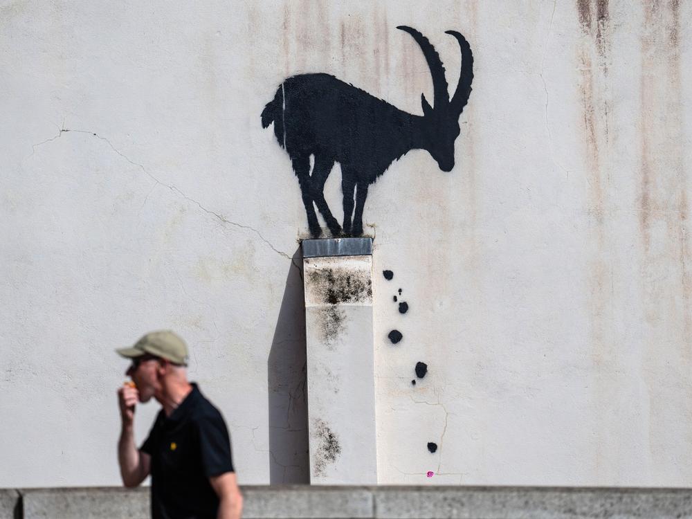A man eats an apple as he walks past a mural depicting a goat, purportedly by the street artist Banksy, on August 5, 2024 in the Richmond borough of London, England. 