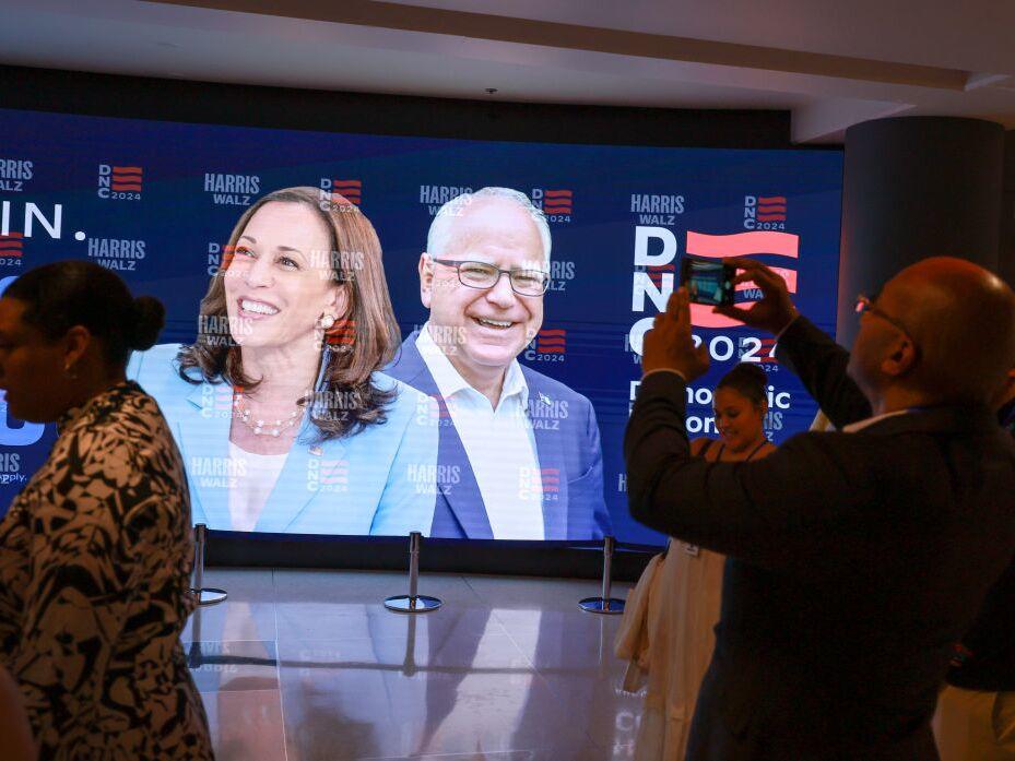 People stand in front of a sign featuring Democratic presidential candidate Vice President Kamala Harris and Democratic Vice presidential candidate Minnesota Gov. Tim Walz at the United Center before the start of the Democratic National Convention Friday in Chicago.