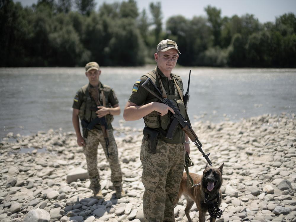 Ukrainian border guards pose with their dog on a pebble beach on the Tisza River bordering Romania, in Velykyi Bychkiv, Ukraine, on July 10.